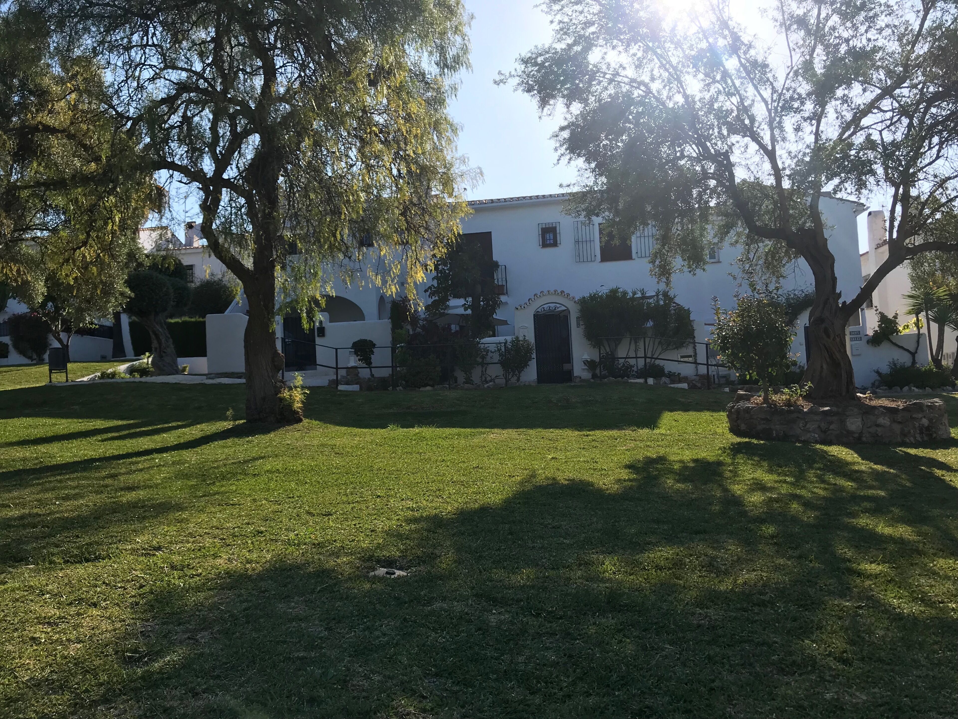 A white building with a gated entrance, surrounded by well-maintained grass and trees.
