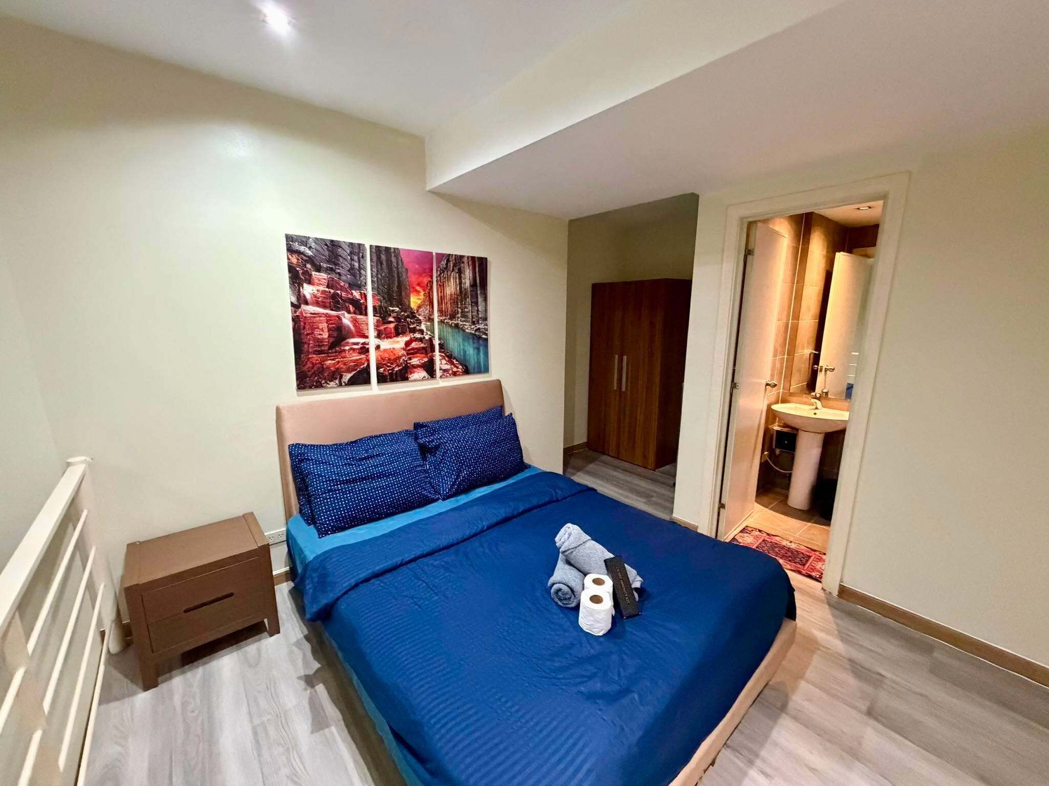 A bedroom with a bed, a nightstand, a bathroom with a sink, and a door leading to another room.