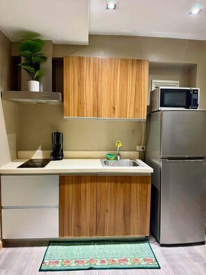 Una cocina compacta con armarios de madera, un refrigerador de acero inoxidable, un microondas y un lavamanos.