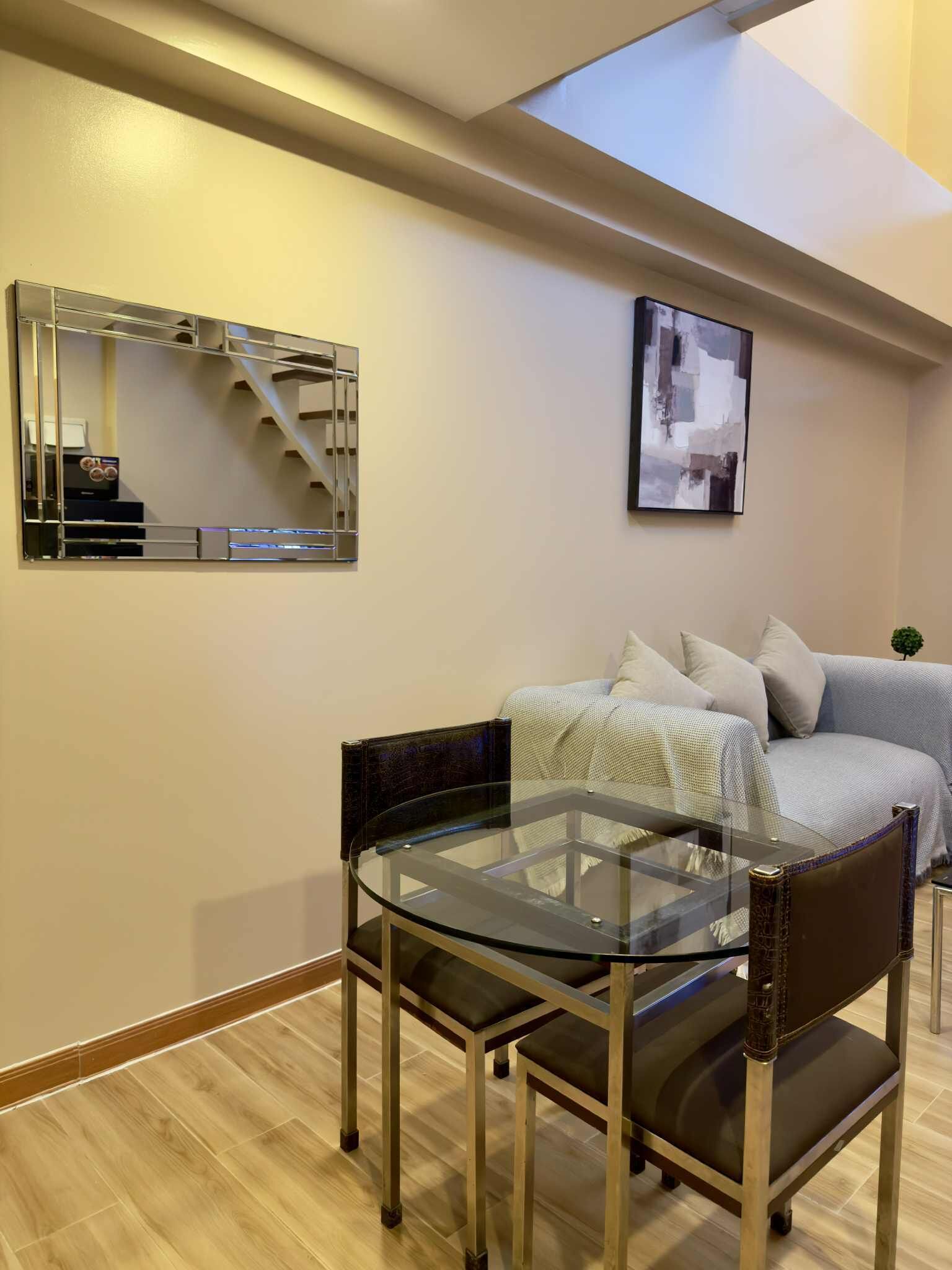 Una sala de estar moderna con una mesa y sillas de vidrio, un sofá, un espejo y un cuadro en la pared.