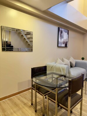 A modern living room with a glass table and chairs, a sofa, a mirror, and a painting on the wall. - The Gramercy Residences  (Makati)