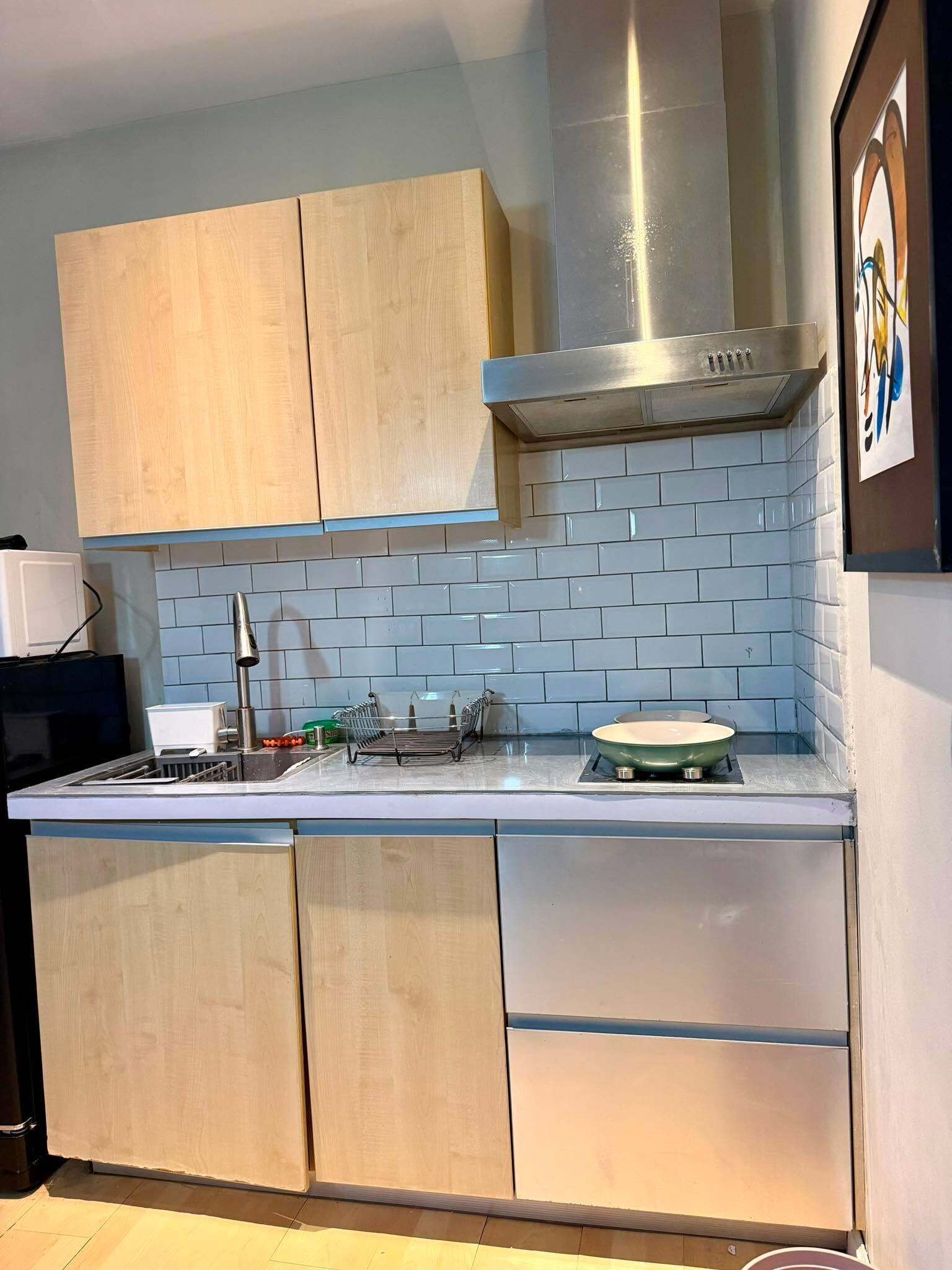 A kitchen with wooden cabinets, a stainless steel range hood, a tiled backsplash, and a countertop with a stove.