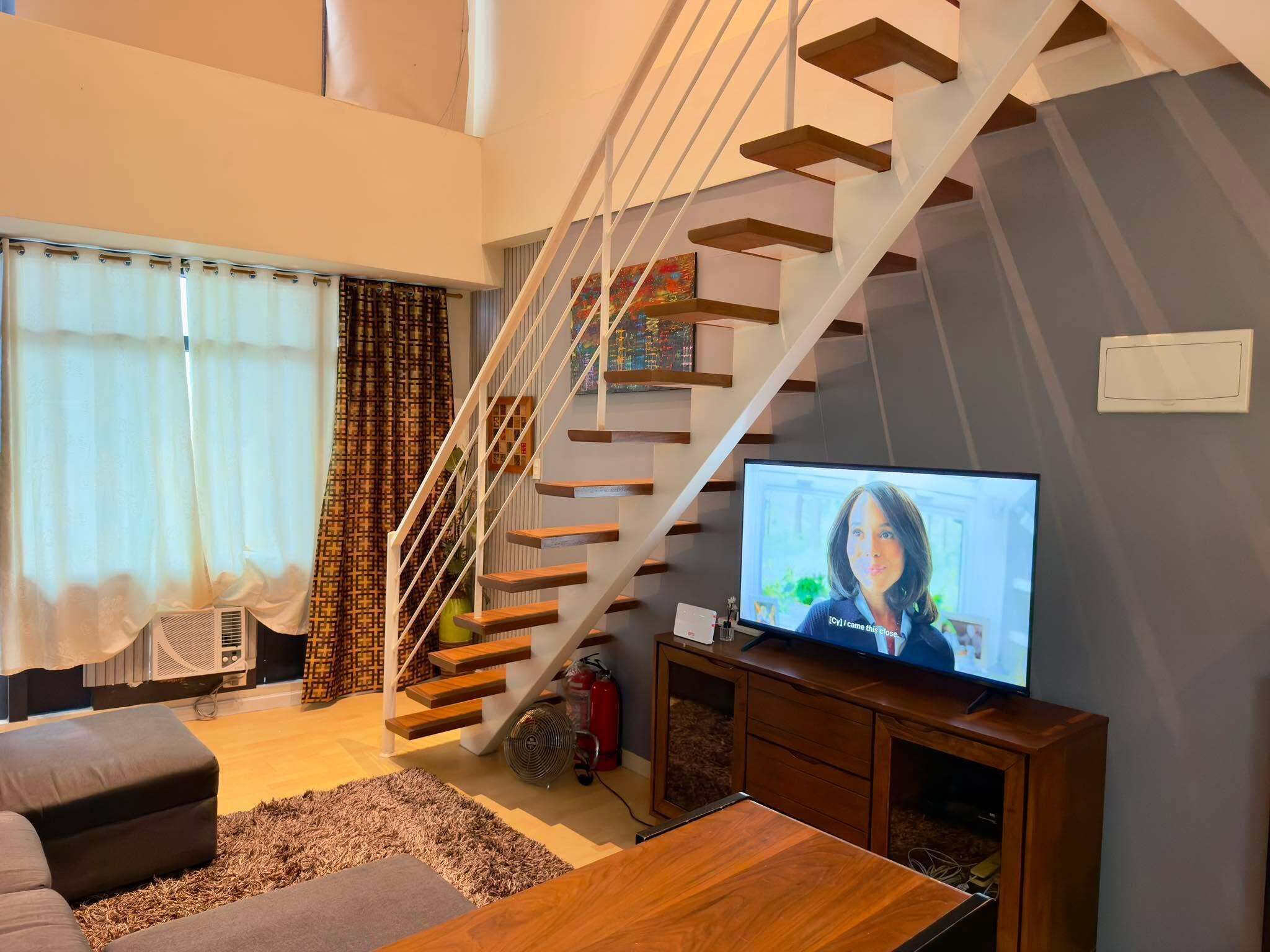 Un salon moderne avec un escalier en bois, un téléviseur à écran plat et un canapé.