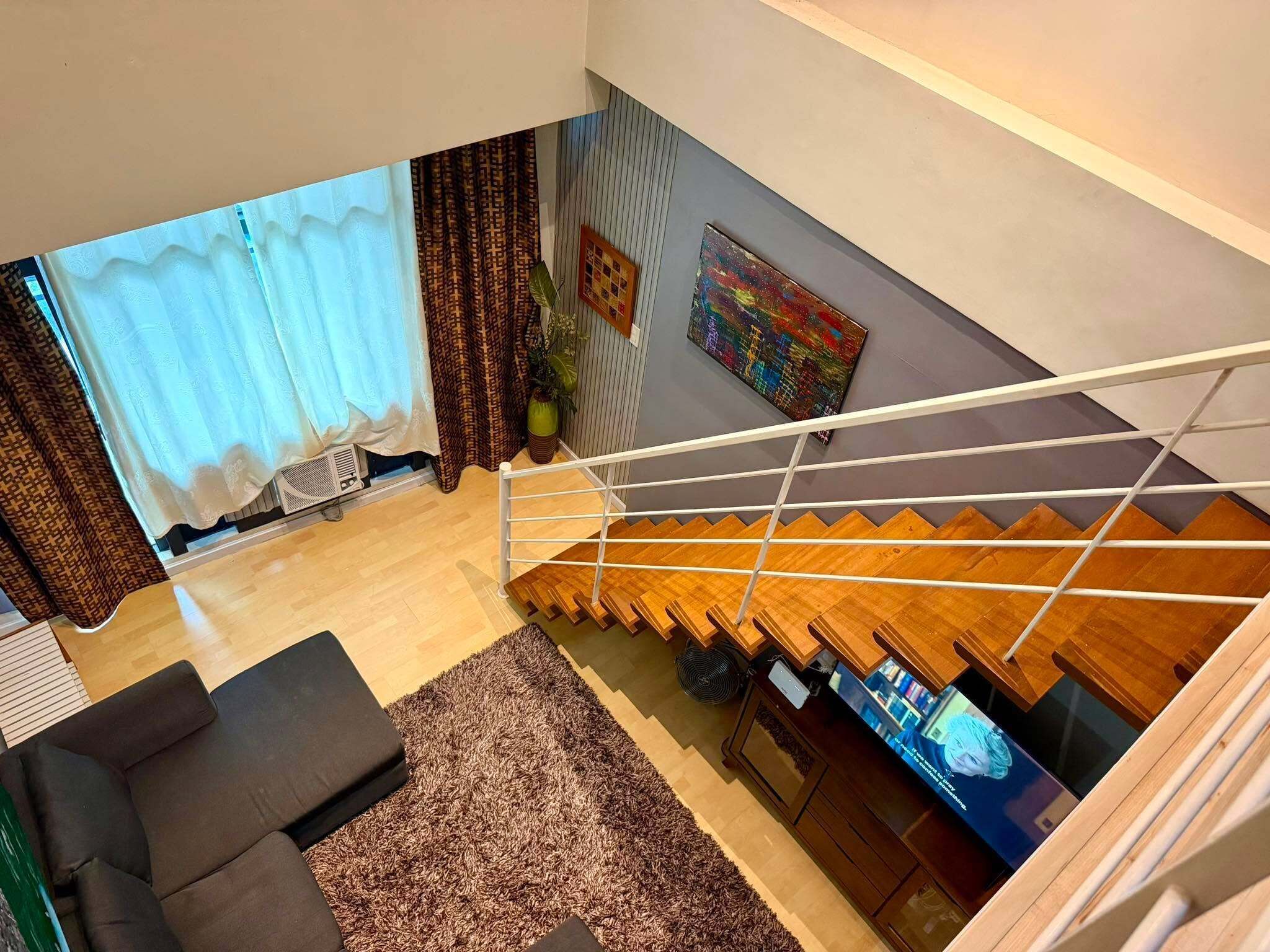 Una sala de estar moderna con una escalera que sube a un nivel superior, un sofá, una alfombra y un cuadro en la pared.