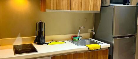 A modern kitchen with wooden cabinets, a stainless steel refrigerator, a microwave, and a sink with a yellow towel.