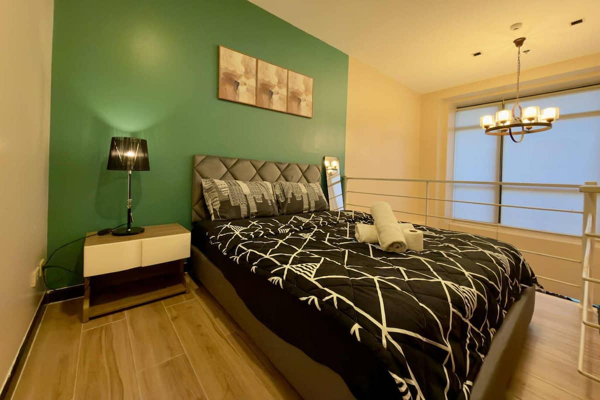 Un dormitorio con cama, mesita de noche, lámpara, candelabro y ventana.