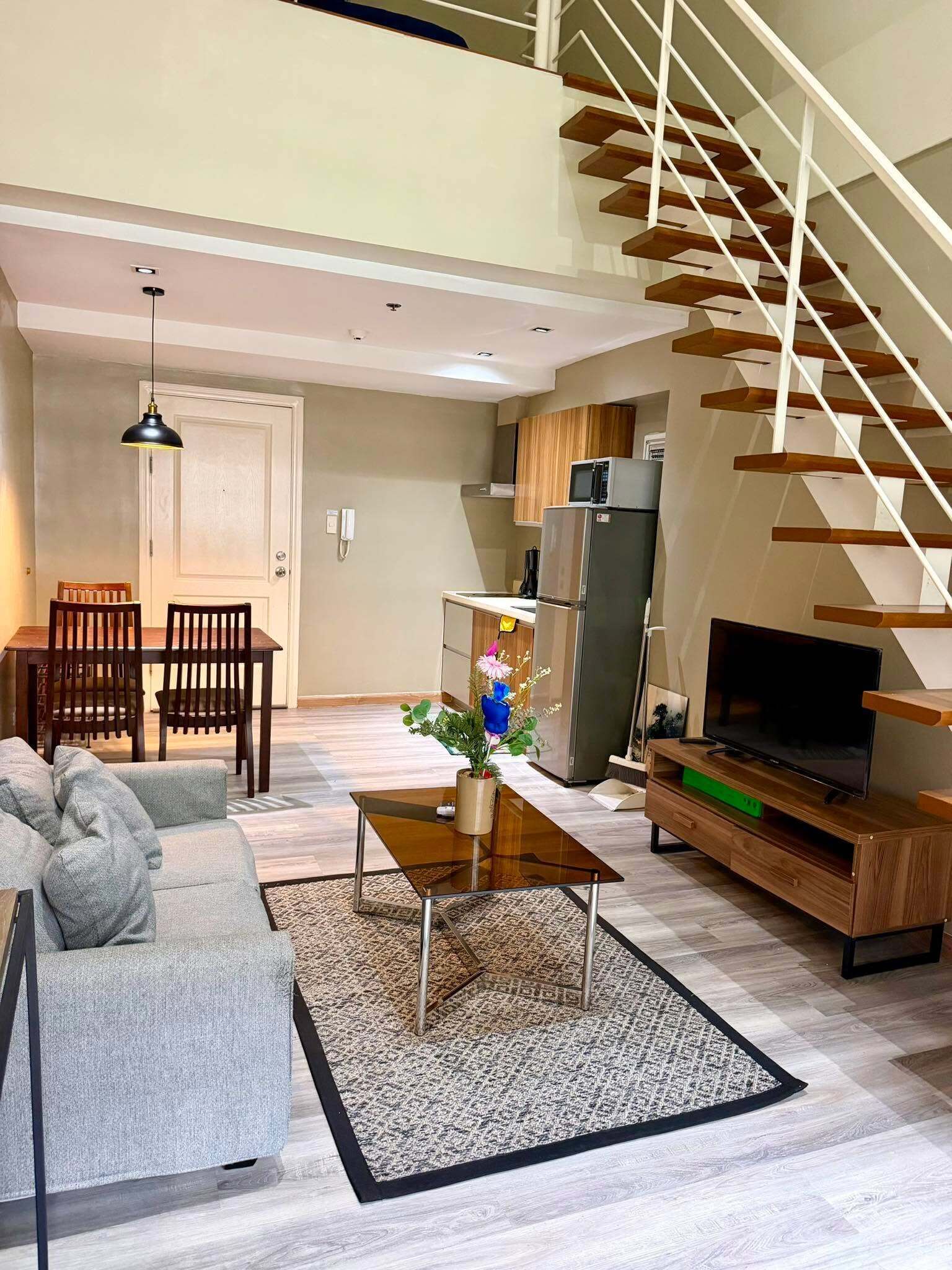 A modern living room with a sofa, coffee table, and TV. A staircase leads to an upper level.