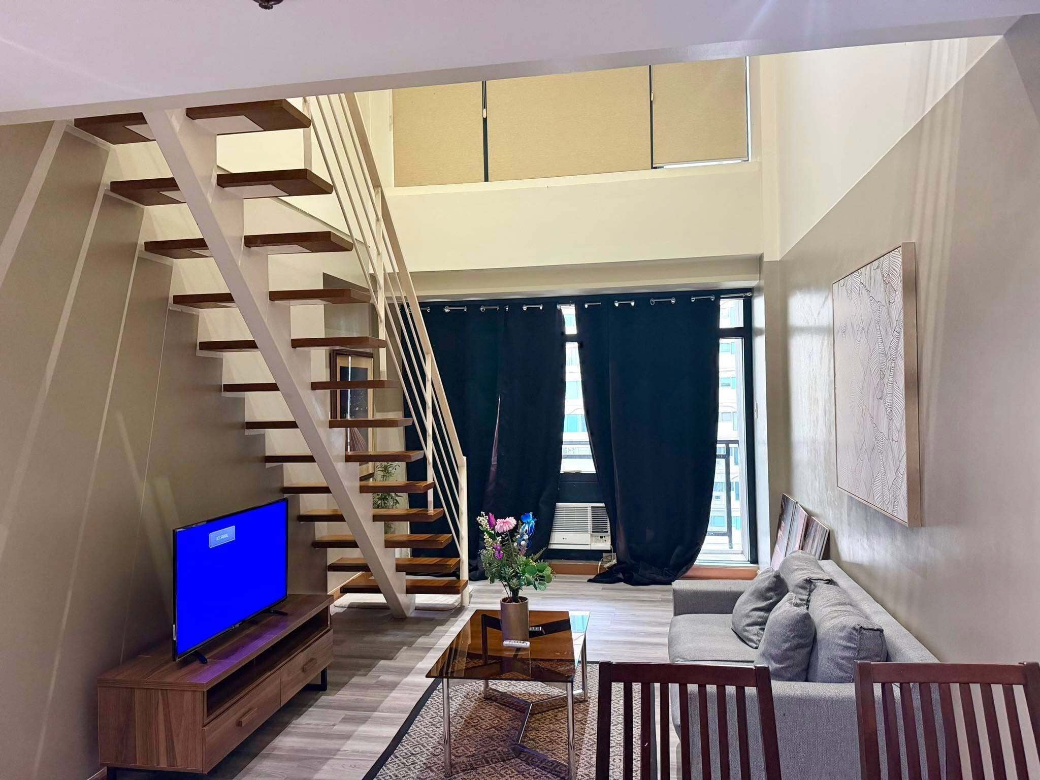 A modern living room with a wooden staircase, a flat-screen TV, a coffee table, and a sofa.