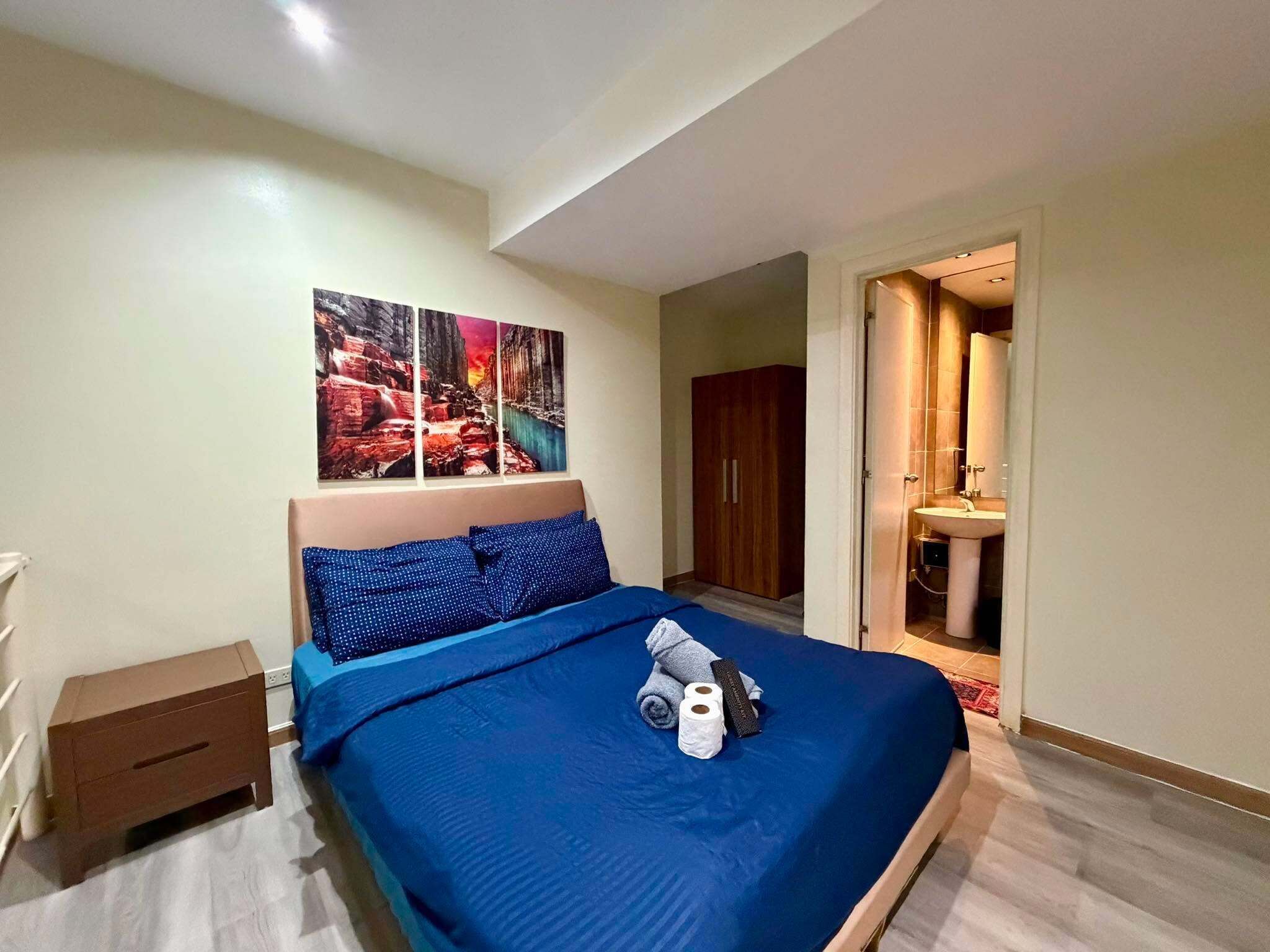 Ein Schlafzimmer mit einem großen Bett, einem Nachttisch, einem Holzschrank und einem durchgehenden Türrahmen einsehbaren Badezimmer.