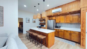 A modern kitchen with wooden cabinets, a central island with bar stools, a built-in oven, and pendant lighting.
