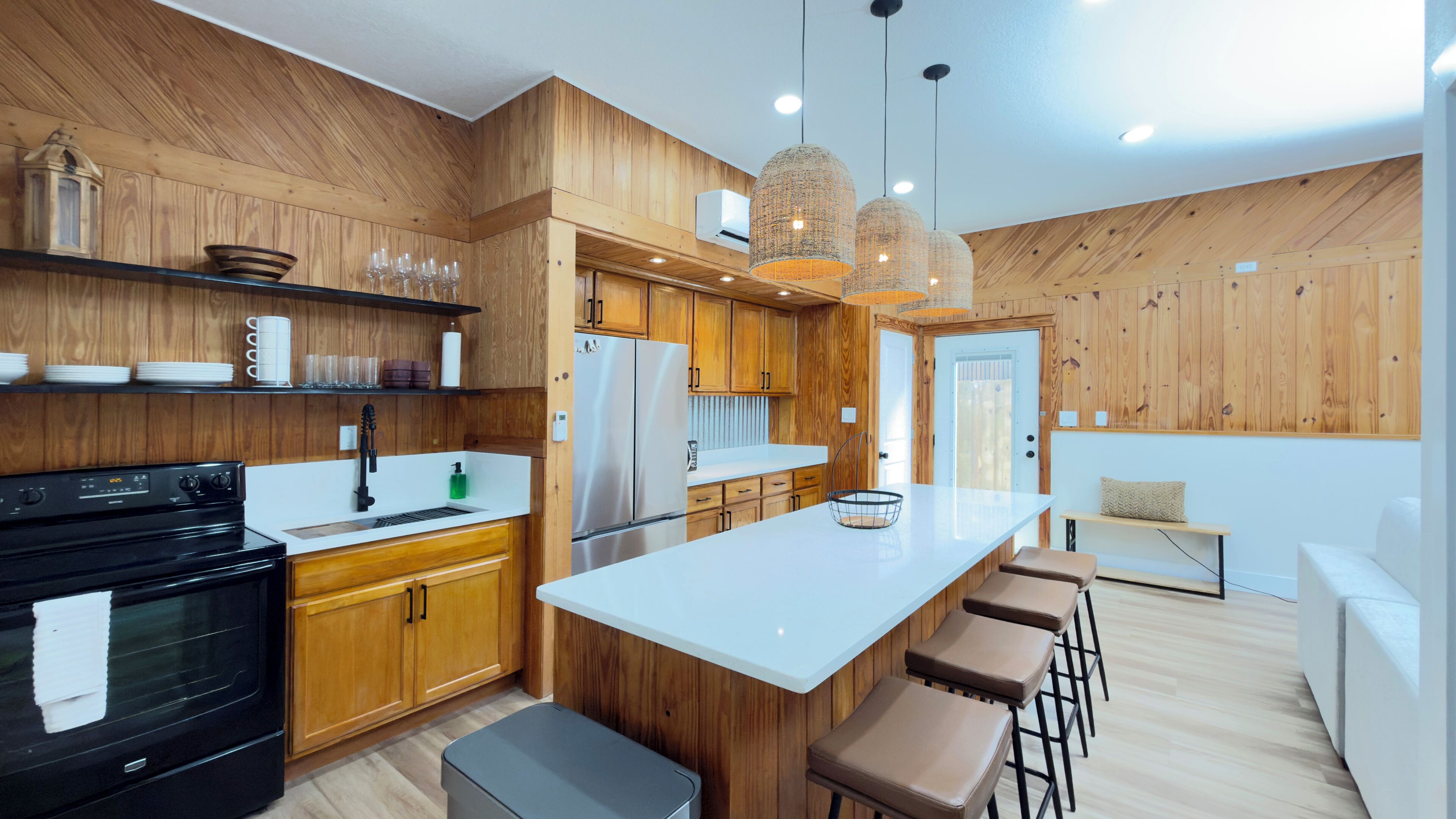 A modern kitchen with wooden cabinetry, a central island with bar stools, a black stove, and pendant lighting.