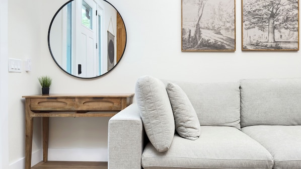 A living room with a round mirror, a wooden desk, a light-colored sofa, and two framed pictures on the wall. - Gorgeous Newly Renovated Getaway 2BR/ 2BA near Blue Spring State Park (Orange City)