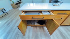 A kitchen with a white countertop, wooden cabinets, and a drawer with kitchen utensils.