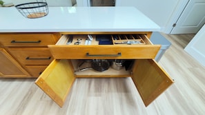 Una cocina con encimera blanca, cajones de madera y una estantería metálica.