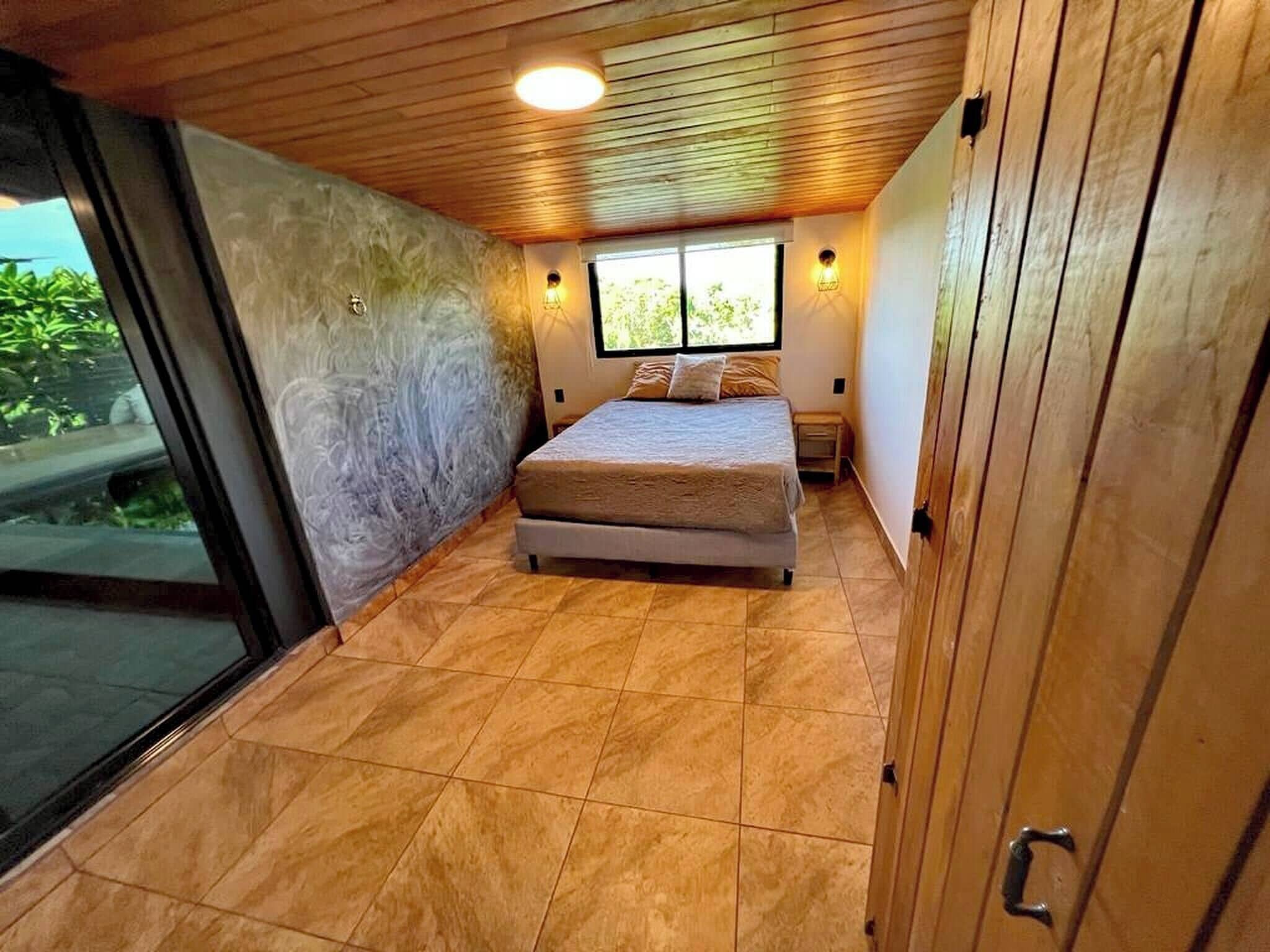 A bedroom with a bed, a window, and a view of greenery outside.