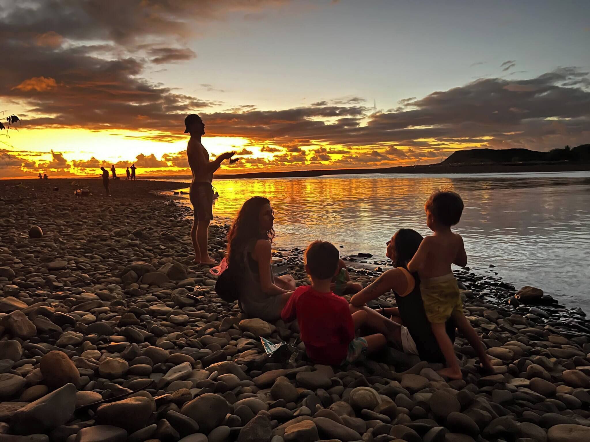 Un grupo de personas en una playa de guijarros durante el atardecer.