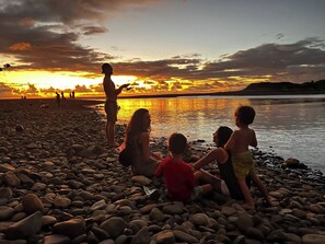 A group of people on a pebbled beach during sunset. - Casa Siempre Verde Ocean View (Nosara)
