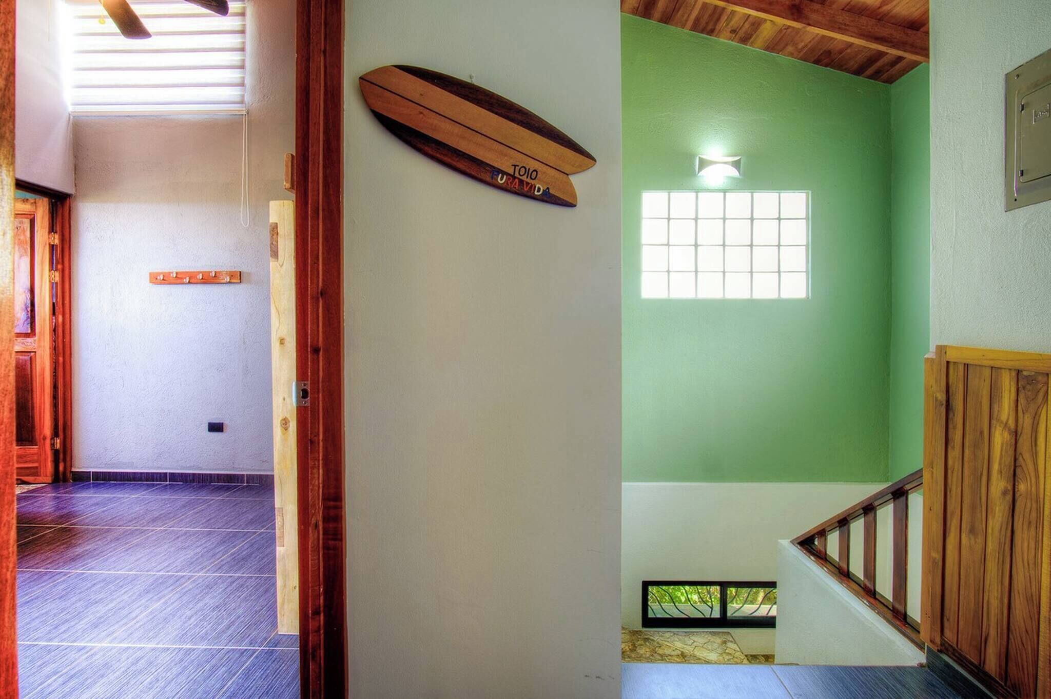 A hallway with a wooden door frame, a wooden object on the wall, and a window with a view of greenery.