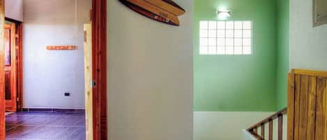 A hallway with a wooden door frame, a wooden object on the wall, and a window with a view of greenery.