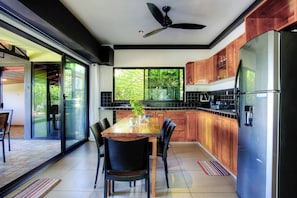 A modern kitchen with a dining area, featuring a large island, wooden cabinets, and a built-in refrigerator. - Casa Siempre Verde Ocean View (Nosara)