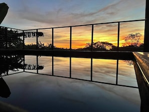 A sunset view through a window with a railing, reflecting the sky and trees. - Casa Siempre Verde Ocean View (Nosara)