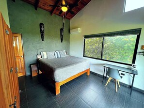 A bedroom with a bed, a desk, a window with a view, and a ceiling fan. - Casa Siempre Verde Ocean View (Nosara)