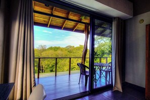 Una habitación con un amplio ventanal corredera que da a un balcón exterior con vistas a zonas verdes.