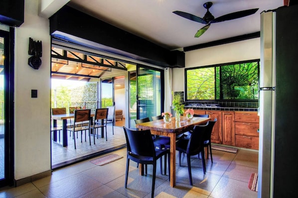 An open-plan living area with a dining table, chairs, and a kitchen area. - Casa Siempre Verde Ocean View (Nosara)