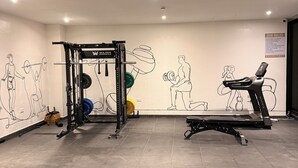 A gym with exercise equipment, a wall with fitness illustrations, and a treadmill. - BridgeView Cantonments (Accra)