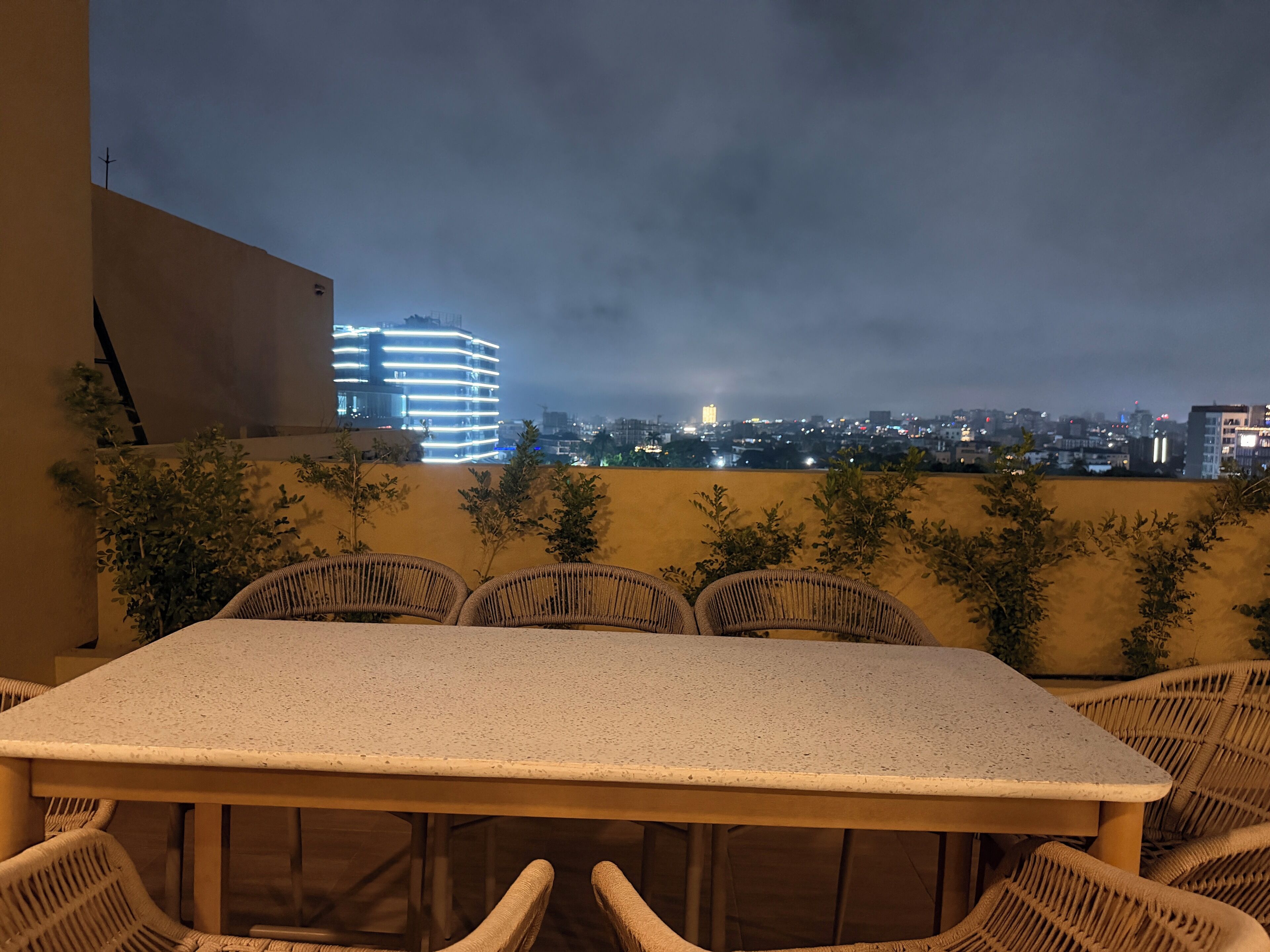 Una terraza con mesa y sillas, con vistas a un paisaje urbano nocturno.