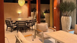A dining area with a round table and chairs, a bench, and a large potted plant. - BridgeView Cantonments (Accra)