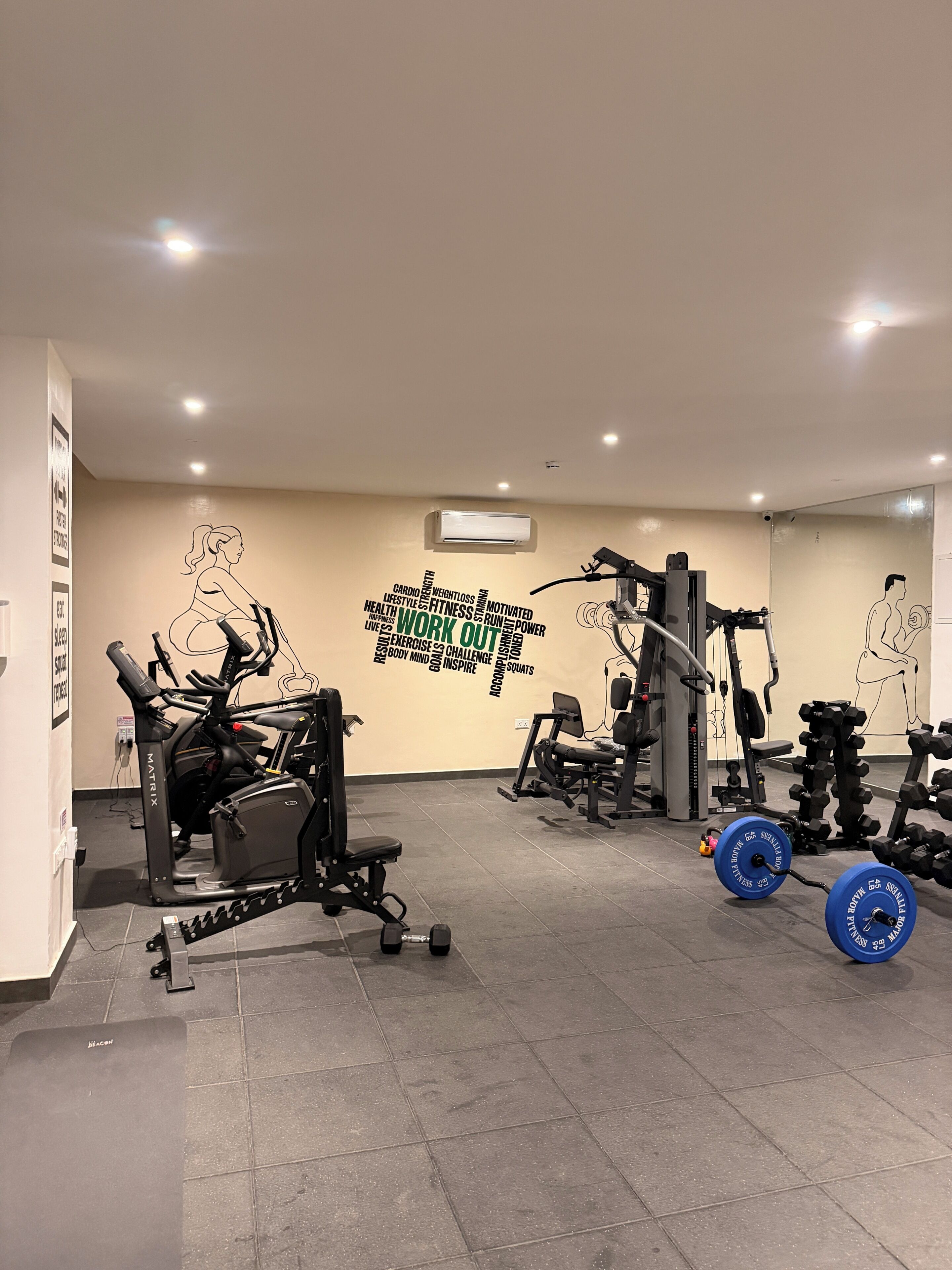 Un gimnasio con máquinas de cardio, equipo de levantamiento de pesas y decoración mural motivacional.