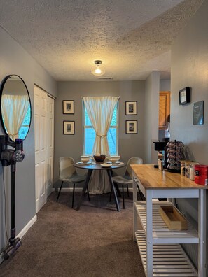 A dining area with a round table, chairs, a coffee machine, and a vacuum cleaner. - Charming 2BR Indianapolis Retreat for Extended Stays (Indianapolis)