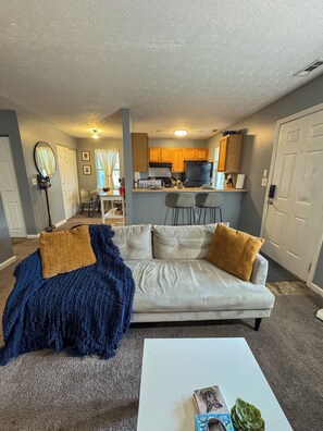 A living room with a sofa, coffee table, and a kitchen in the background. - Charming 2BR Indianapolis Retreat for Extended Stays (Indianapolis)