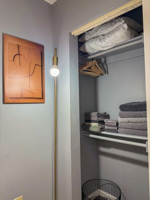 A closet with hanging clothes and folded towels. - Charming 2BR Indianapolis Retreat for Extended Stays (Indianapolis)