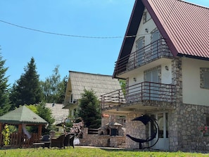 A two-story building with a stone facade, a balcony with red railings, and a small outdoor seating area with chairs and a table.