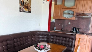 A dining area with a wooden table and cushioned chairs, a kitchen with wooden cabinets and a red accent wall, and a framed picture on the wall.