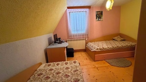 A small bedroom with two single beds, a desk, a radiator, and a window with blinds.