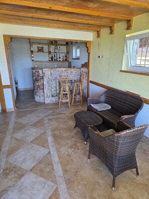 A room with a wicker sofa, a bar area with stools, and a tiled floor.