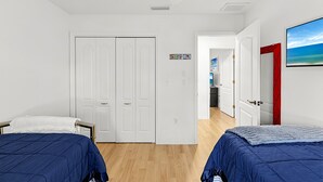 A bedroom with two beds, a wardrobe, a ceiling fan, and a door leading to a bathroom.