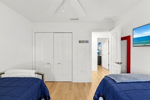 Une chambre avec deux lits, une armoire, un ventilateur de plafond et une porte donnant sur une salle de bain.