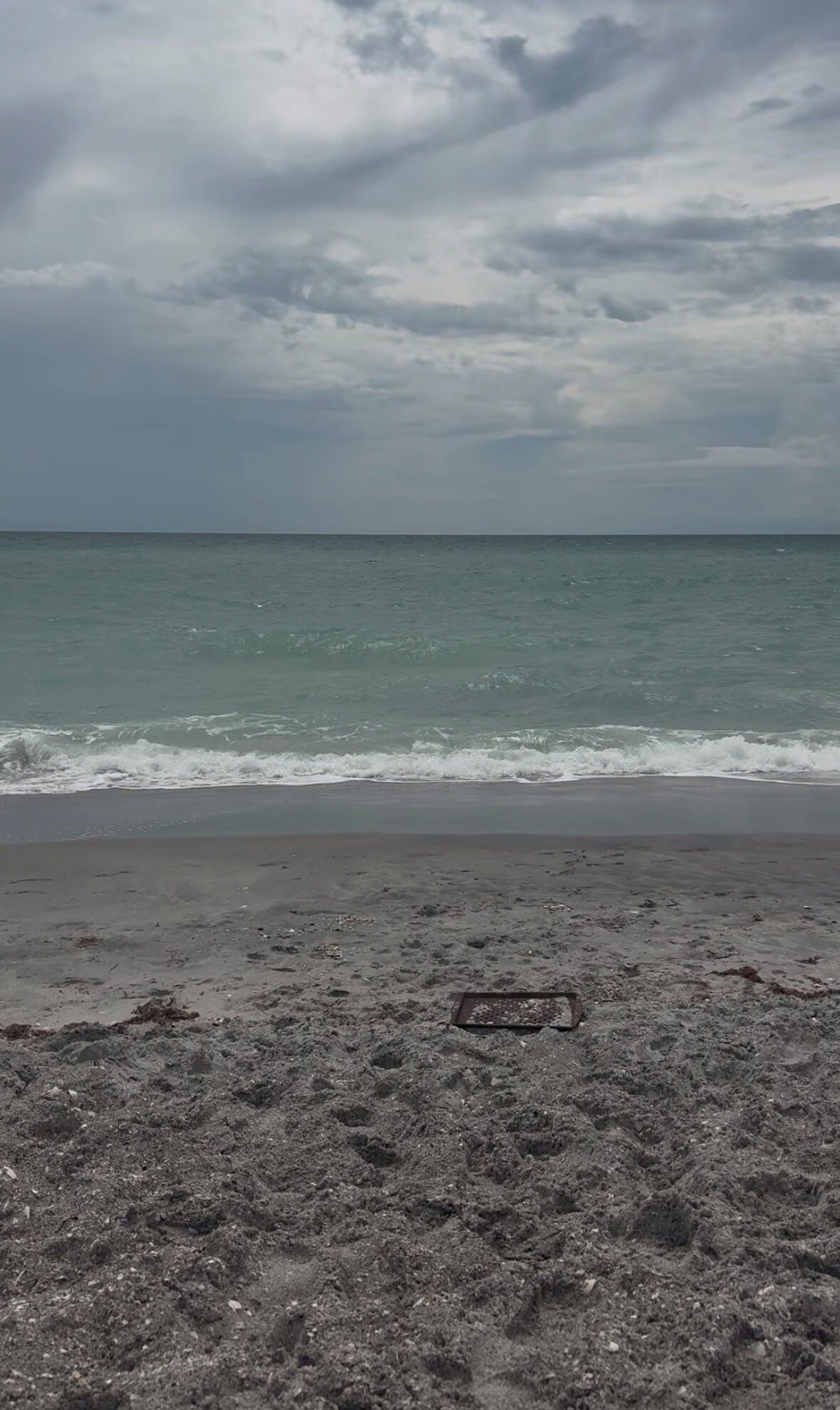 Ein Strand mit einem Abflussgitter im Vordergrund und einem bewölkten Himmel.