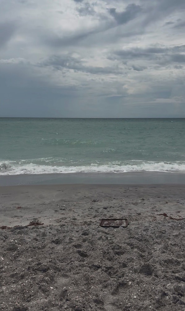 Une plage avec une grille d’évacuation au premier plan et un ciel nuageux au-dessus.
