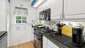 A compact kitchen with white cabinets, a black microwave, a stove, and a coffee maker.