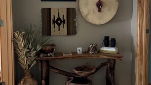 Eine hölzerne Bank mit einem geflochtenen Korb darunter, einem gerahmten Kunstwerk darüber und einem runden Dekorationsobjekt an der Wand.