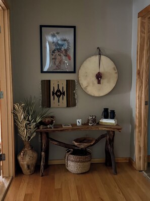 Eine hölzerne Bank mit einem geflochtenen Korb darunter, einem gerahmten Kunstwerk darüber und einem runden Dekorationsobjekt an der Wand.
