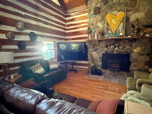Ein gemütliches Blockhaus-Interieur mit Kamin aus Stein, Ledermöbeln und einem Fernseher.