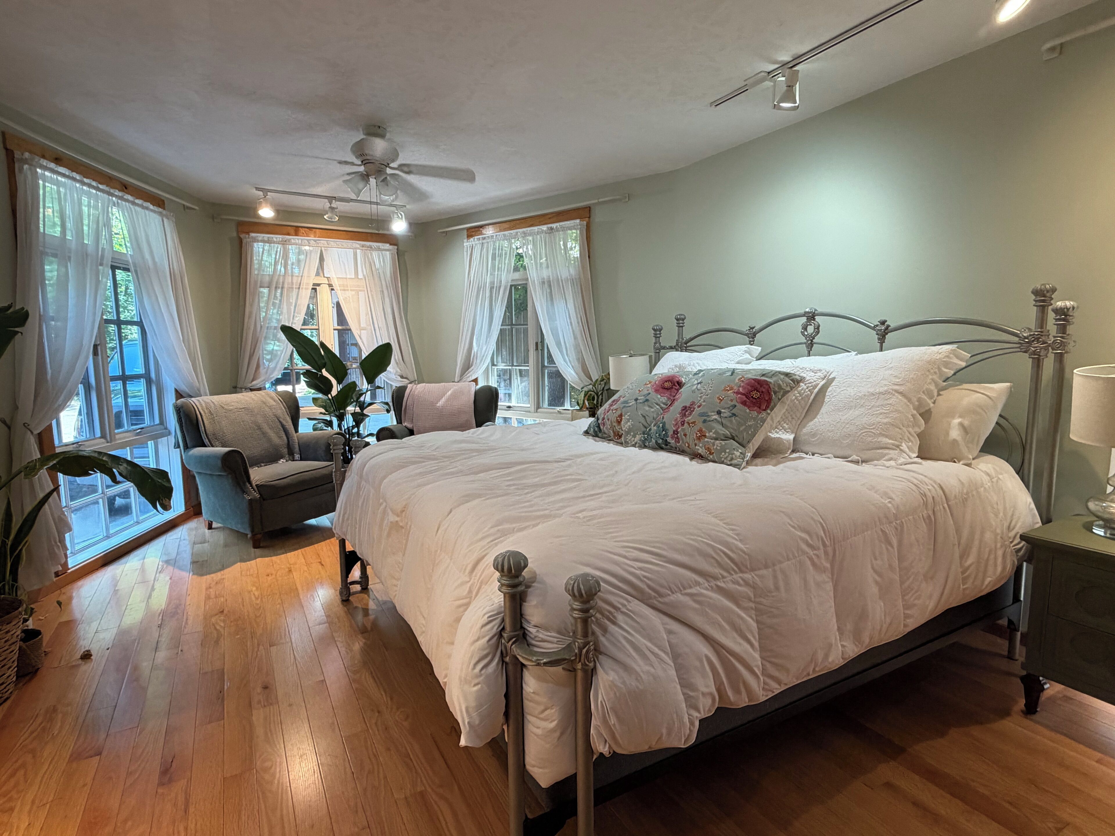 A bedroom with a large bed, a chair, a ceiling fan, and a window with curtains.