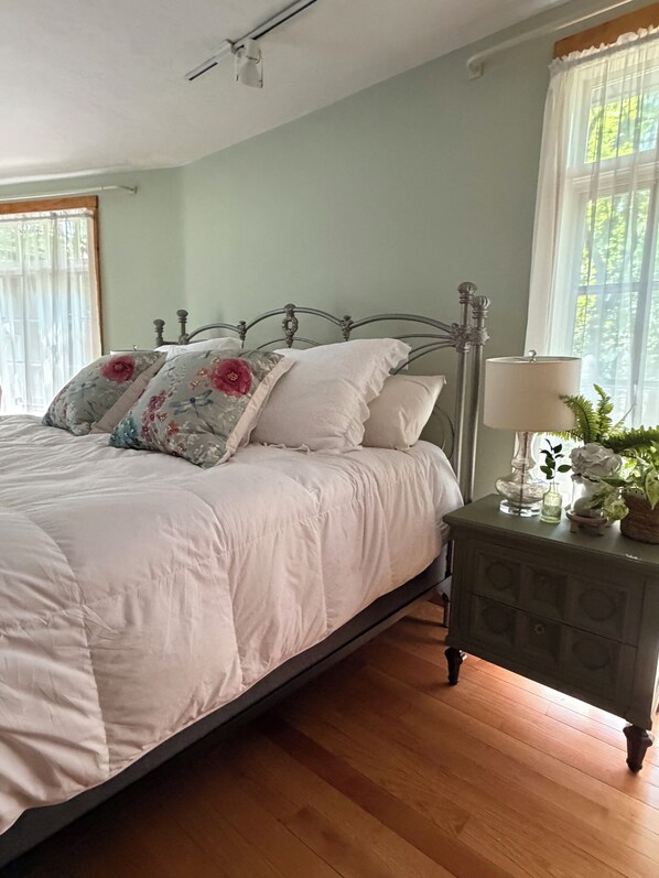 A bedroom with a bed, a nightstand with a lamp, and a window with curtains.