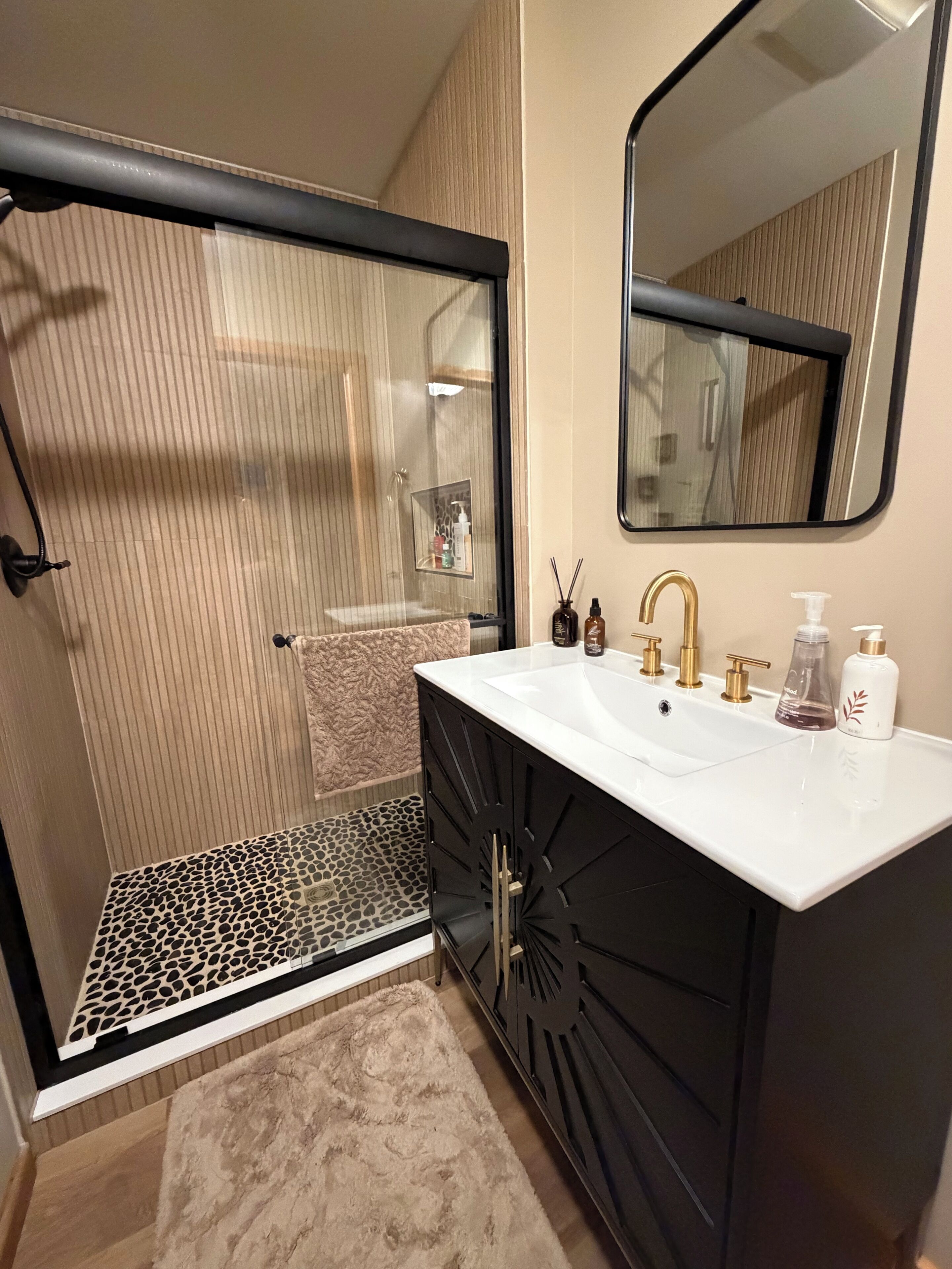 Une salle de bain dotée d’une douche à parois de verre, d’un lavabo blanc avec des accessoires dorés et d’un miroir au-dessus du lavabo.